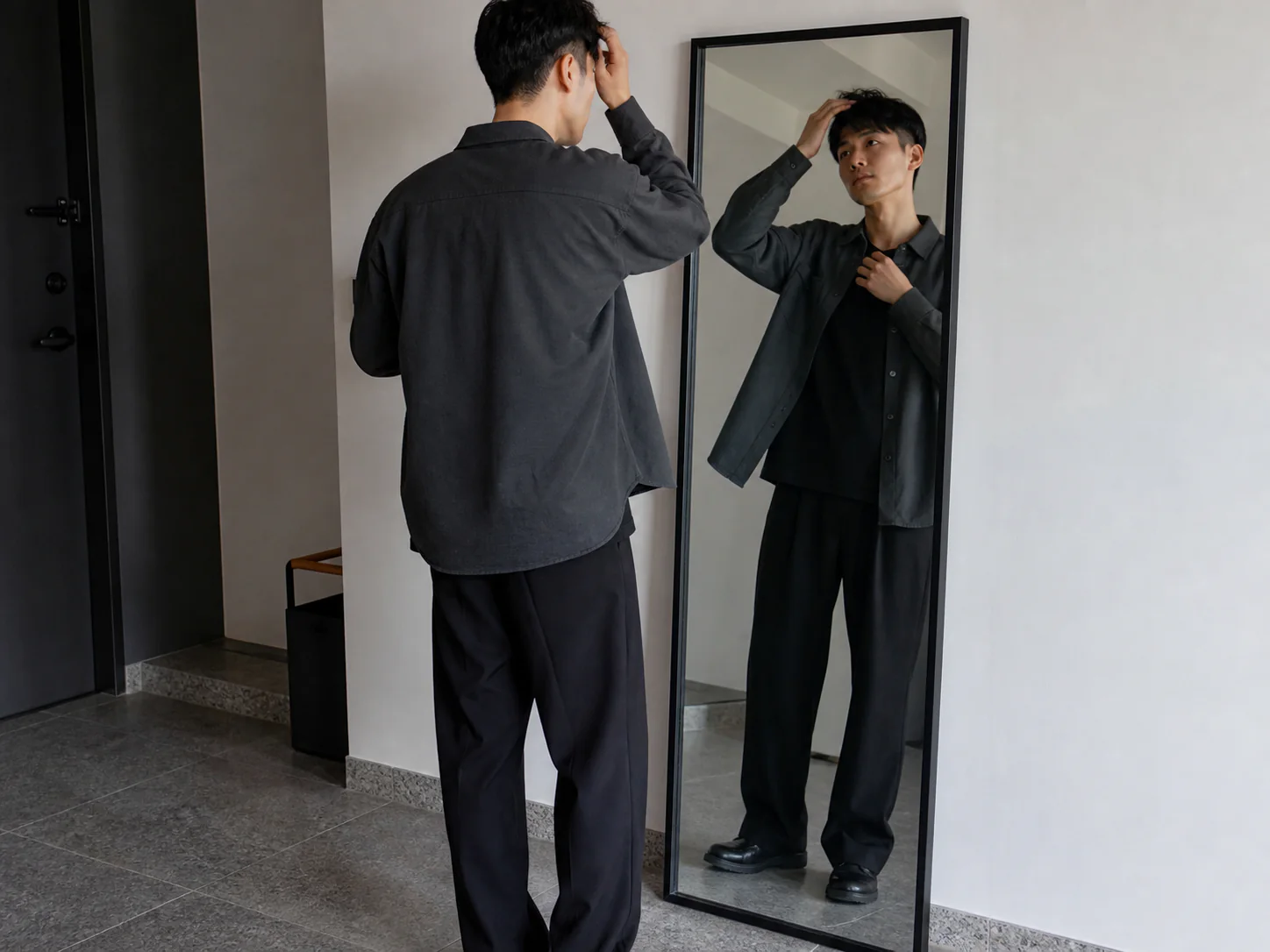 全身鏡で髪と眉と襟元を確認する男性
