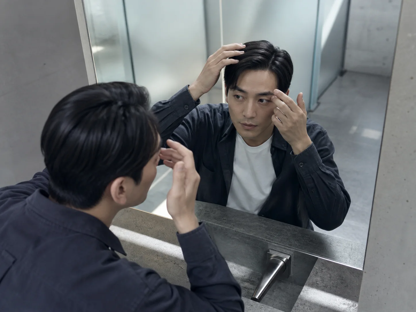 仕事前に洗面鏡で身だしなみを確認する男性